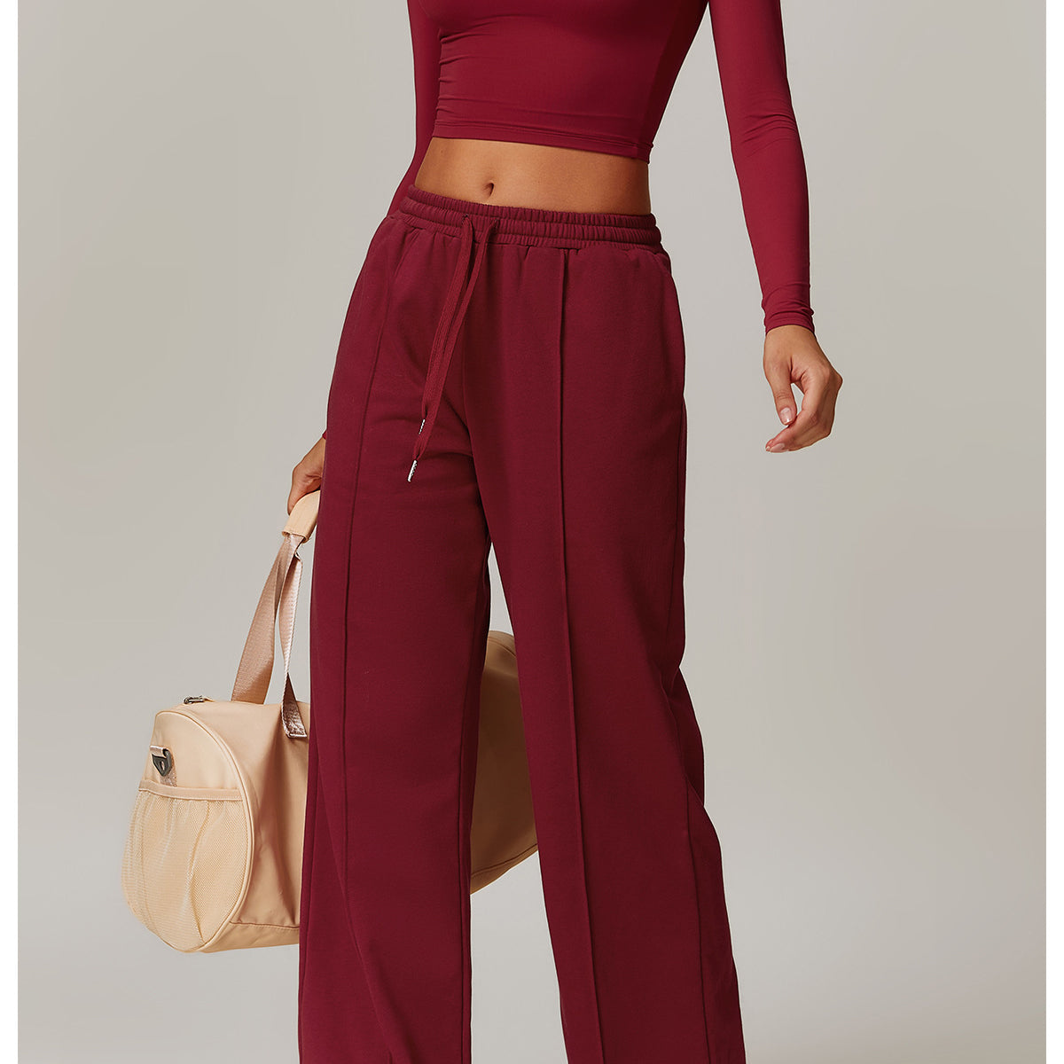 Burgundy crop top and wide-leg pants set, paired with white sneakers and a beige handbag for fashionable fitness attire