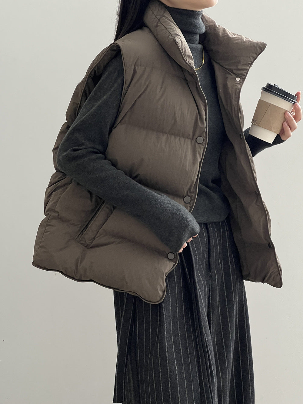 Brown puffy down vest over a dark pinstriped dress in stylish fashion ملابس