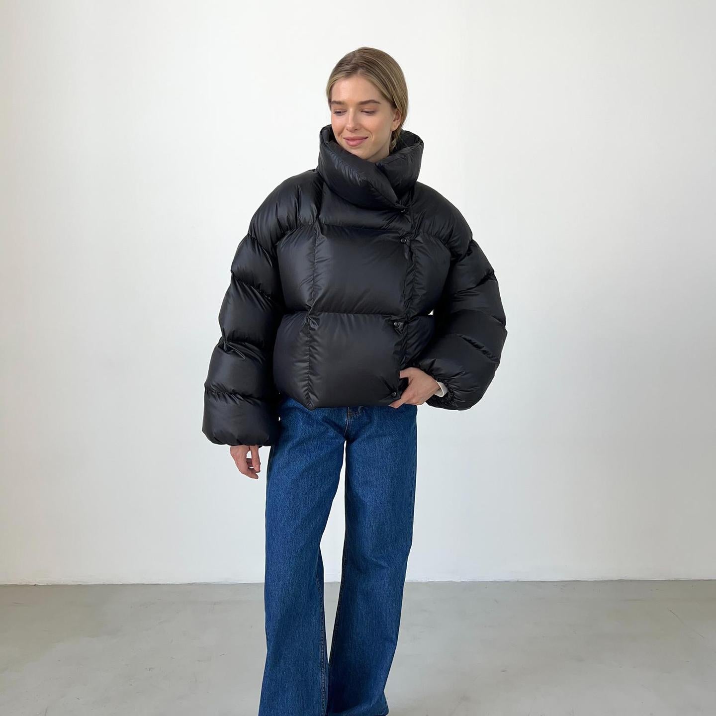 Woman in a black puffer jacket and blue jeans showcasing trendy fashion ملابس style