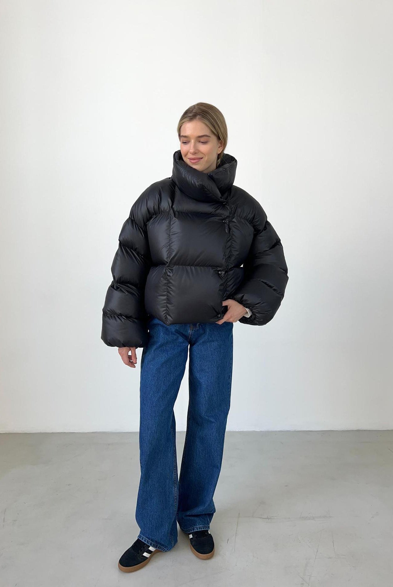 Woman in a black puffer jacket and blue jeans showcasing trendy fashion ملابس style