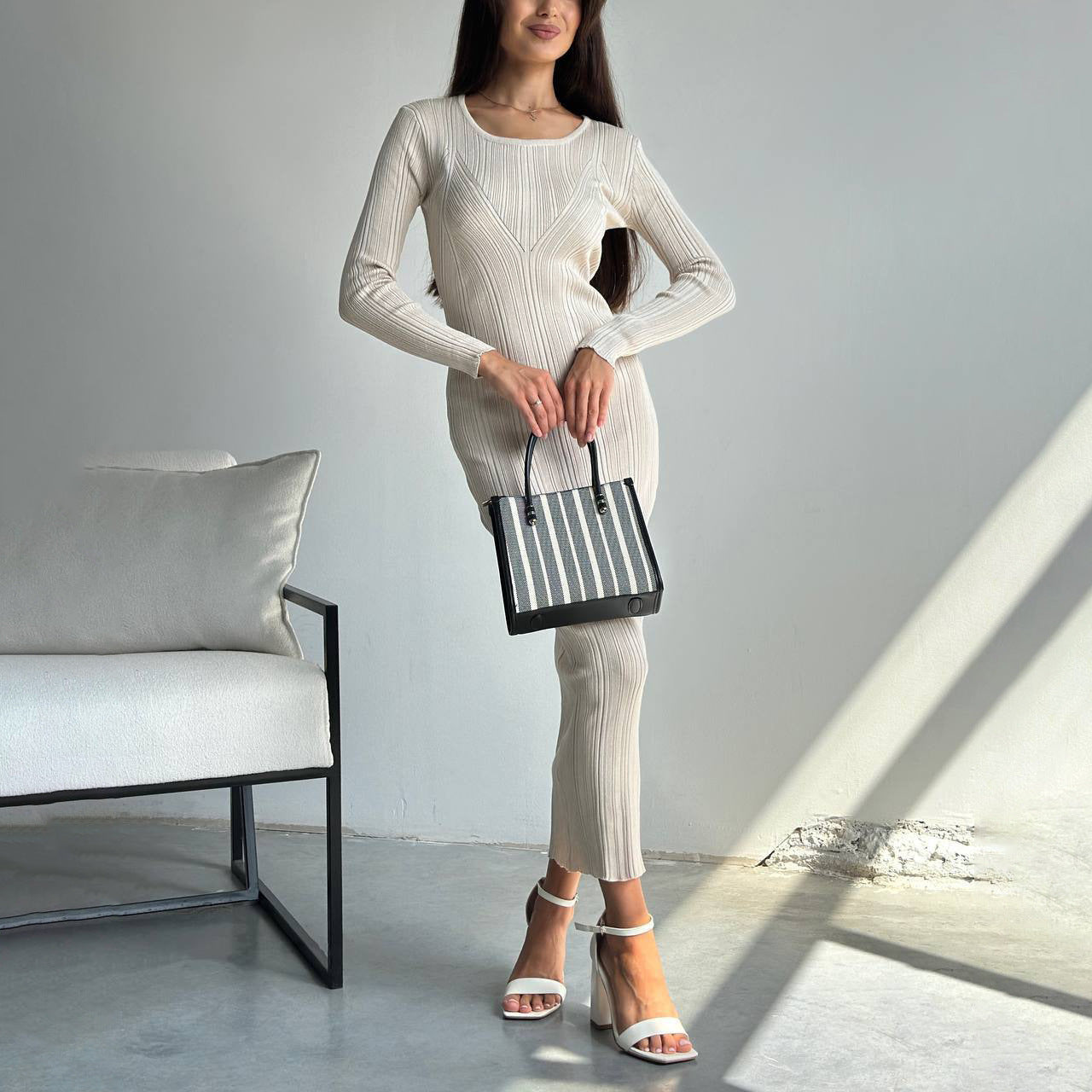 Woman in a ribbed knit dress paired with a striped tote bag showcasing modern fashion ملابس