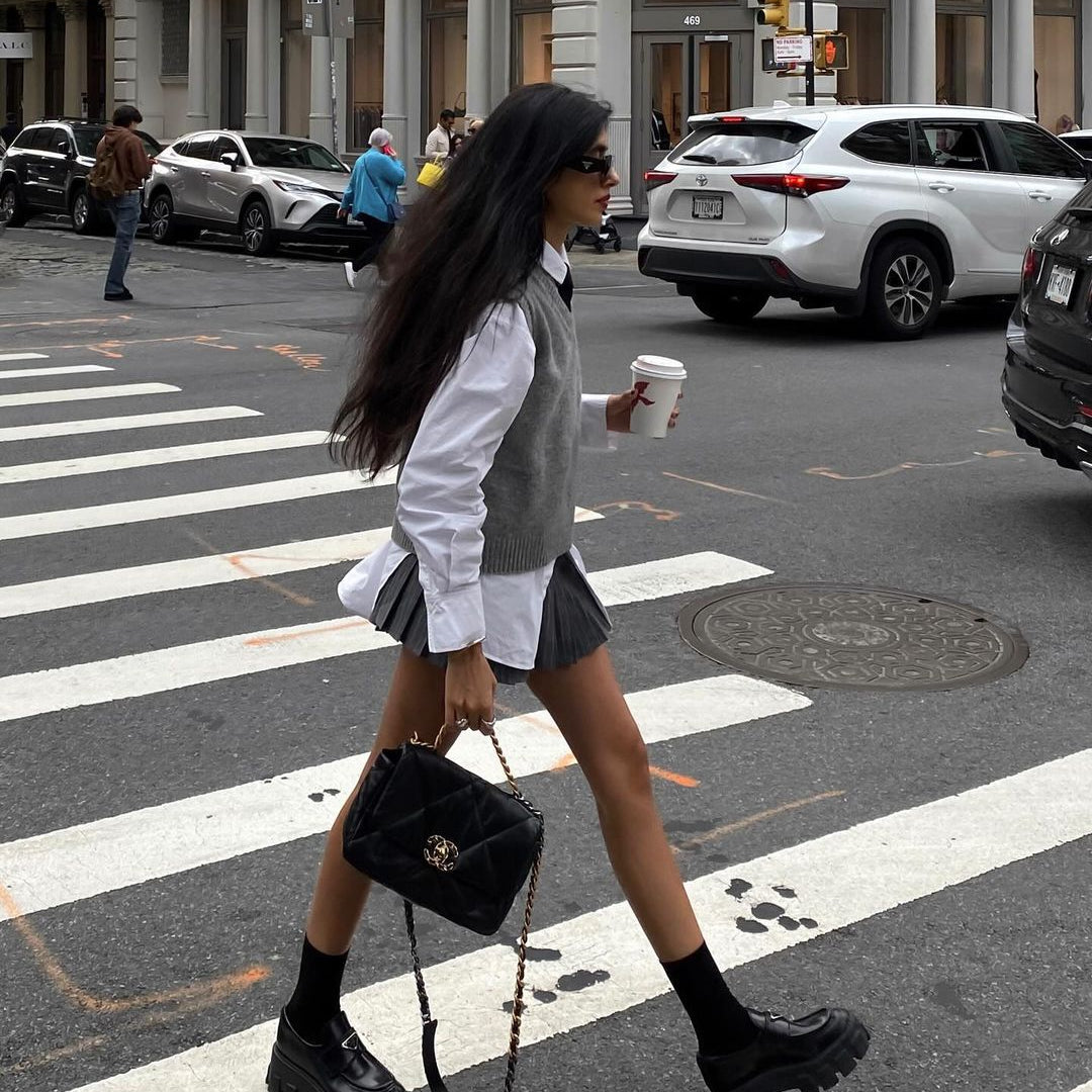 Fashionable woman in white shirt, skirt, chunky boots, and Chanel bag crossing city street