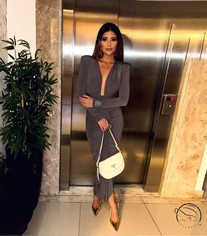 Elegant slim evening dress in gray pleated langry fashion with deep neckline, long sleeves, paired with gold high heels