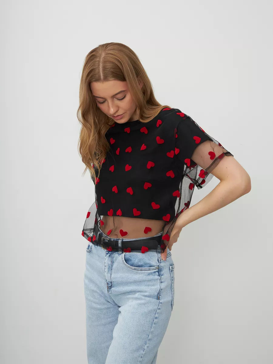 Black mesh crop top with red heart pattern paired with light wash jeans for stylish fashion