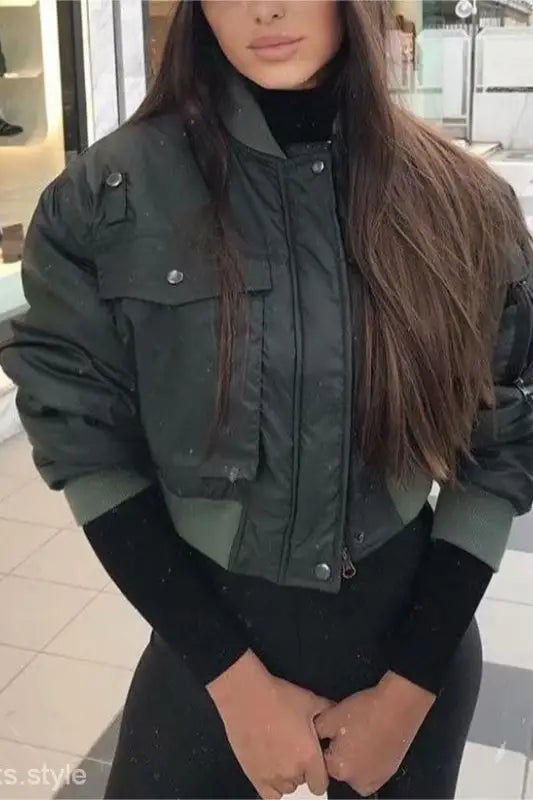 Dark green bomber jacket with pockets and zippers, styled over a black top