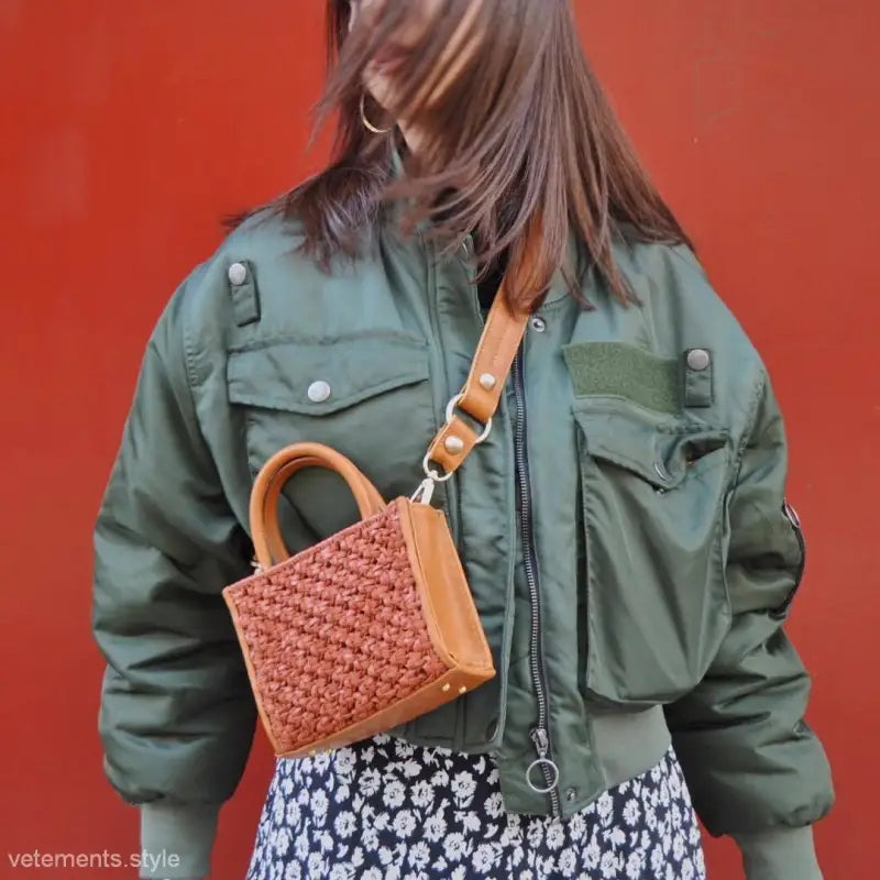 Green bomber jacket over a floral dress, styled with a woven handbag for casual flair