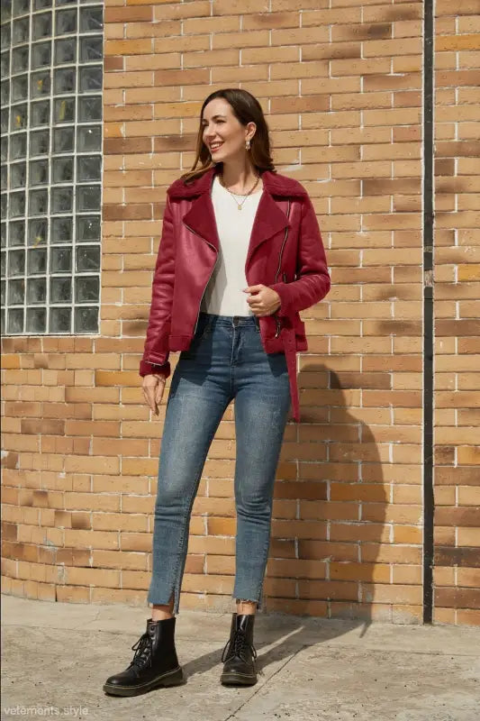 Woman in red shearling jacket and jeans showcasing a stylish army green faux leather jacket with belt closure