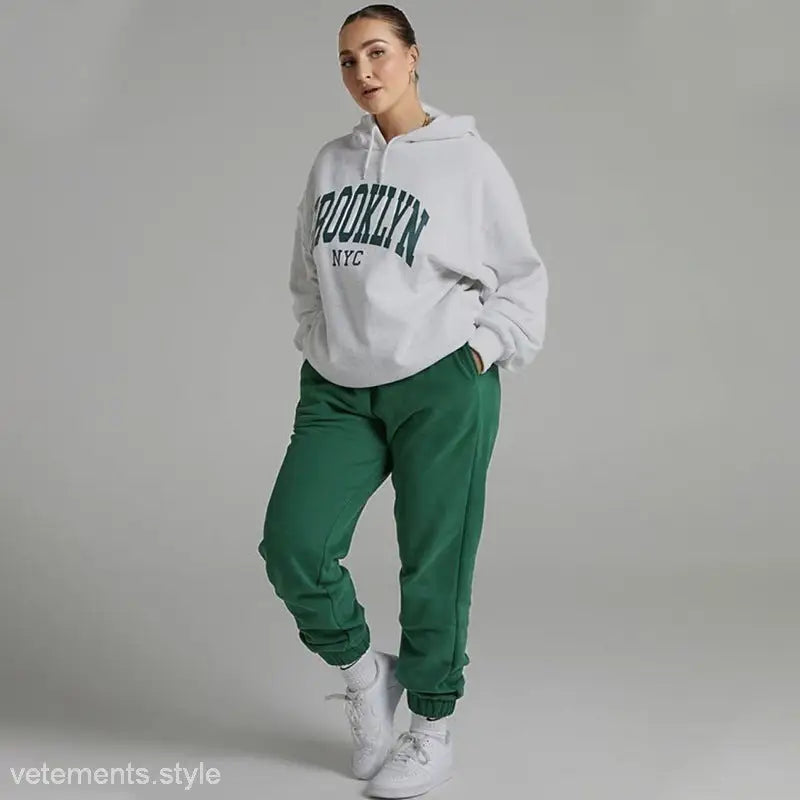 Woman in a Brooklyn sweatshirt set featuring a white hoodie and green sweatpants