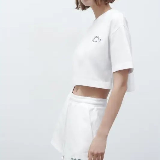 Woman in white crop top and shorts wearing Palo Alto Set styling with text flock shorts