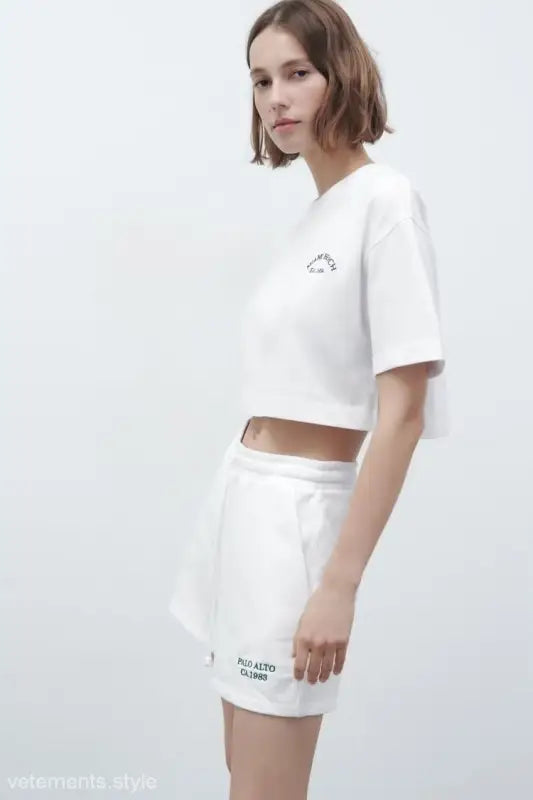 Woman in white crop top and shorts wearing Palo Alto Set styling with text flock shorts