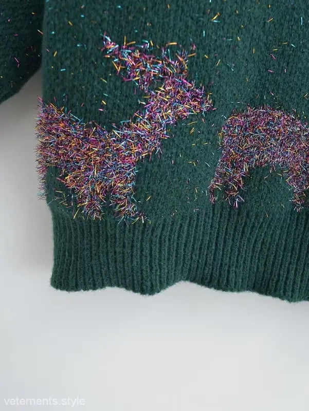 Green knit deer holiday sweater with colorful tinsel decorations for festive occasions