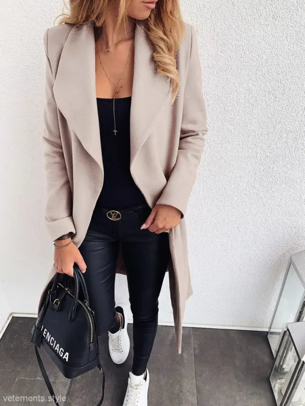 Beige open-front trench coat over black top and pants with white sneakers for fall style