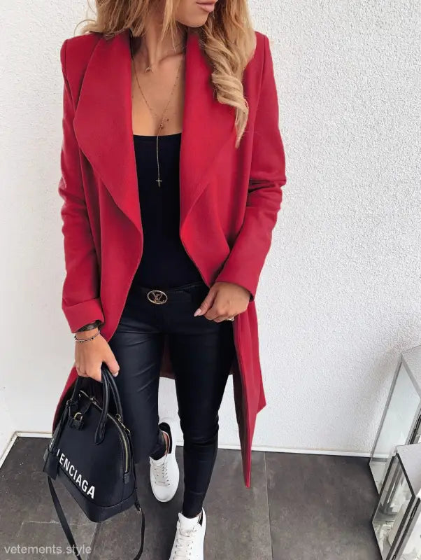 Vibrant red trench coat over black outfit with white sneakers and designer handbag