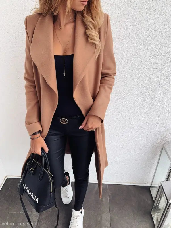Camel-colored trench coat over black outfit with sneakers and Balenciaga handbag