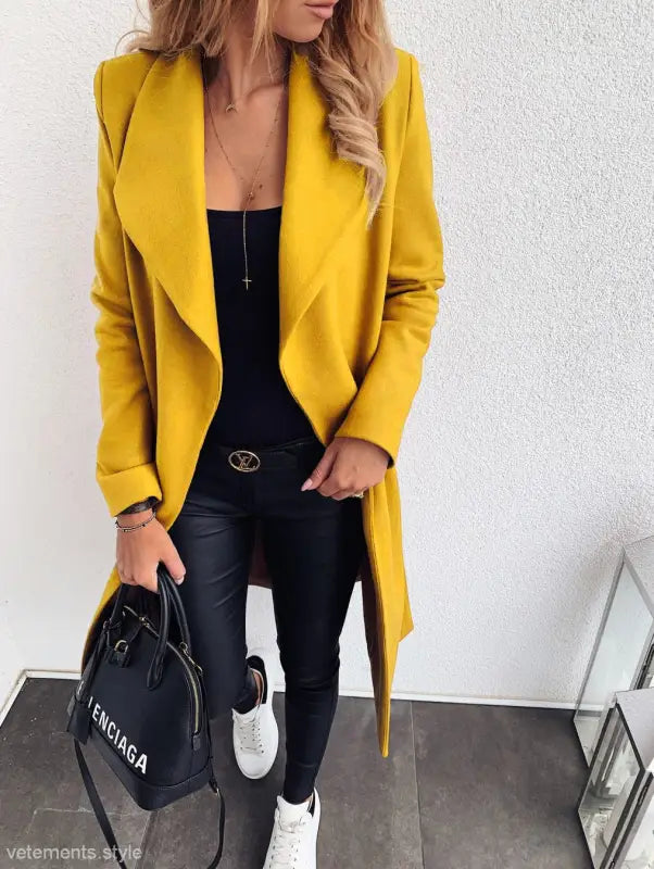 Bright yellow trench coat over black outfit with white sneakers for fall and winter