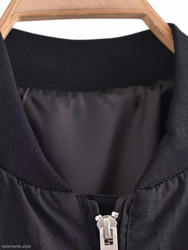 Black short bomber jacket with pocket and tie stand collar on wooden hanger