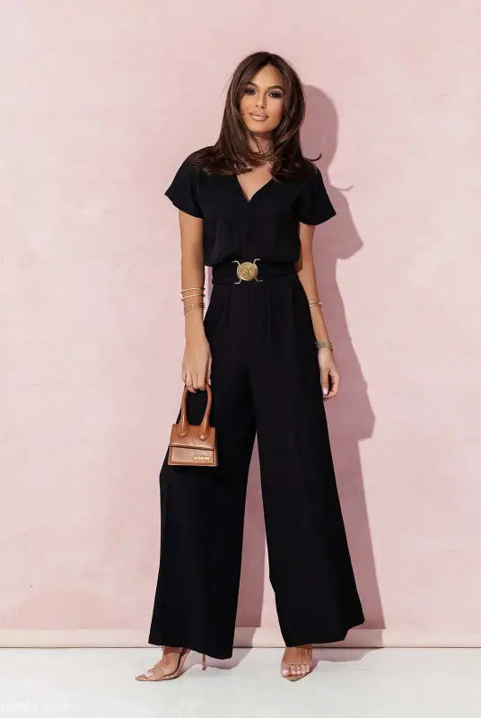 Woman wearing a black wide-leg casual trousers jumpsuit with gold belt and handbag
