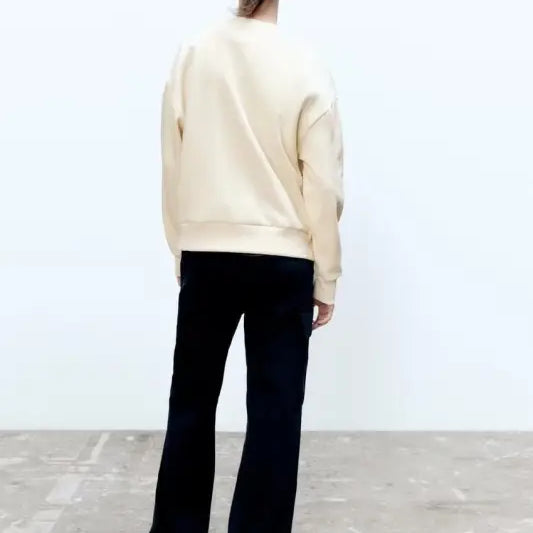 Person in cream-colored girl pattern sweater and black pants, seen from behind