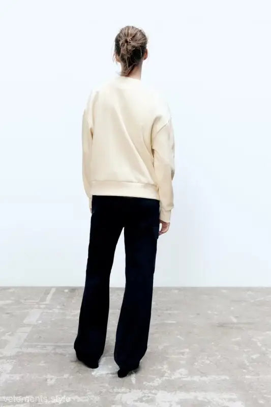 Person in cream-colored girl pattern sweater and black pants, seen from behind