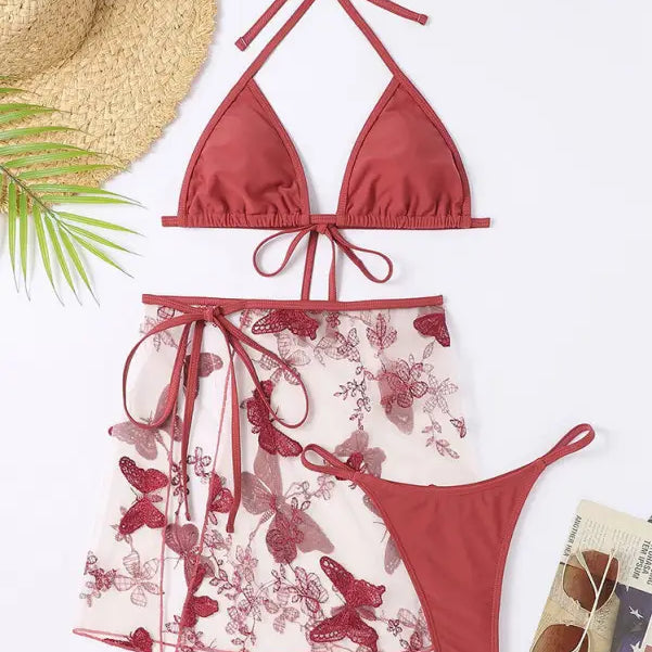 Three-piece red bikini set with a matching sheer floral skirt.