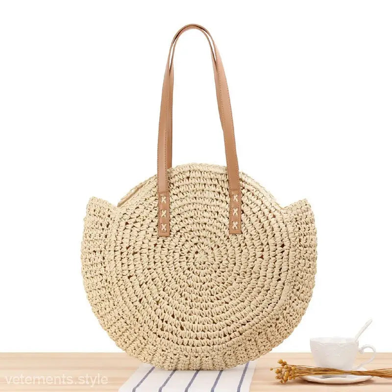 Circular woven straw beach bag with tan leather handles in large striped blue and light brown