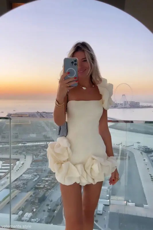 Woman in white floral summer dress with ruffled asymmetrical design and one shoulder sleeve