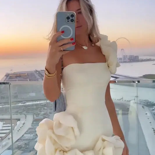 Woman in white ruffled summer dress taking a selfie, showcasing elegant asymmetric design