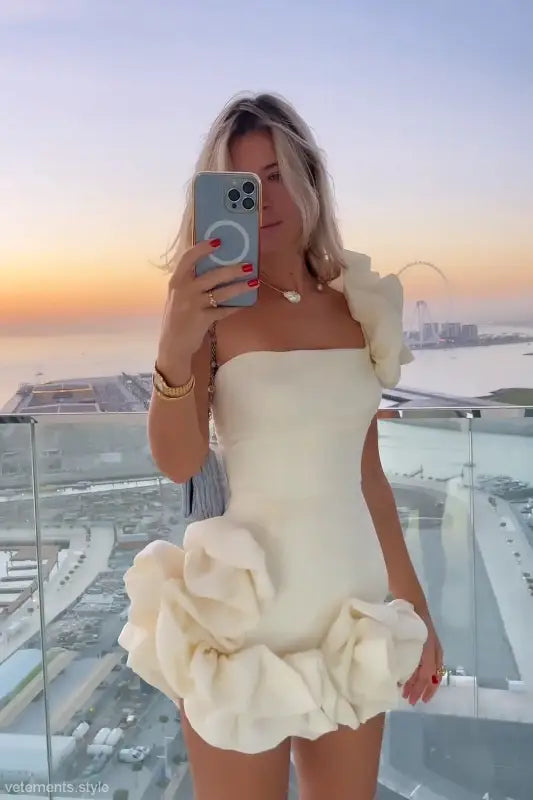 Woman in white ruffled summer dress taking a selfie, showcasing elegant asymmetric design