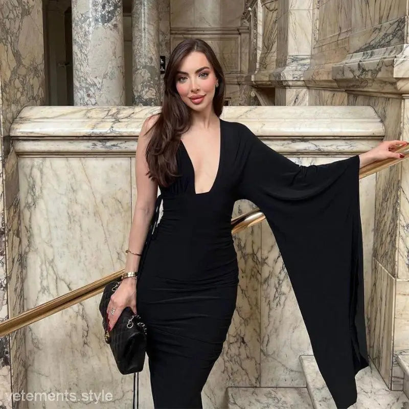 Woman in a sexy low cut backless evening dress with ruched detailing and dramatic sleeve