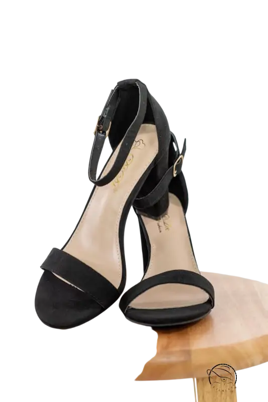 Stylish black heeled sandals with adjustable ankle strap on wood