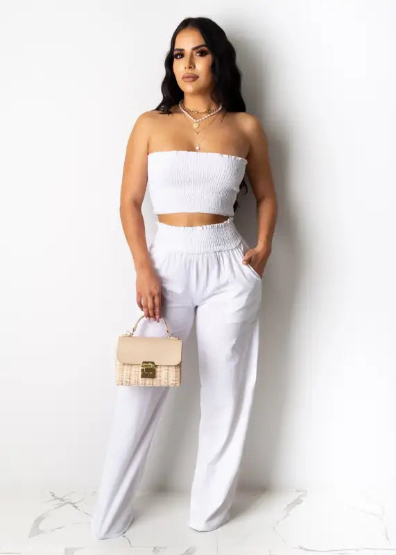 Woman in white crop top and high-waisted pants holding a beige handbag for Berlin summer outfit