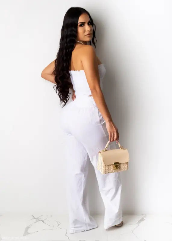 Woman with long dark hair in white summer outfit holding beige handbag for Berlin summer outfit