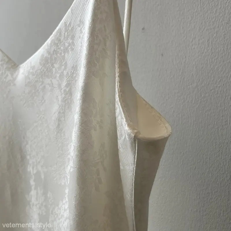 White silk garment hanging on a hook, showcasing elegant jacquard V-neck strap dress design