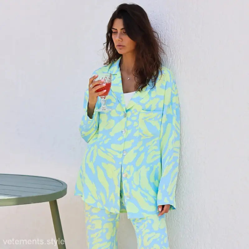 Woman in blue and green patterned long sleeve silk pajamas holding a drink