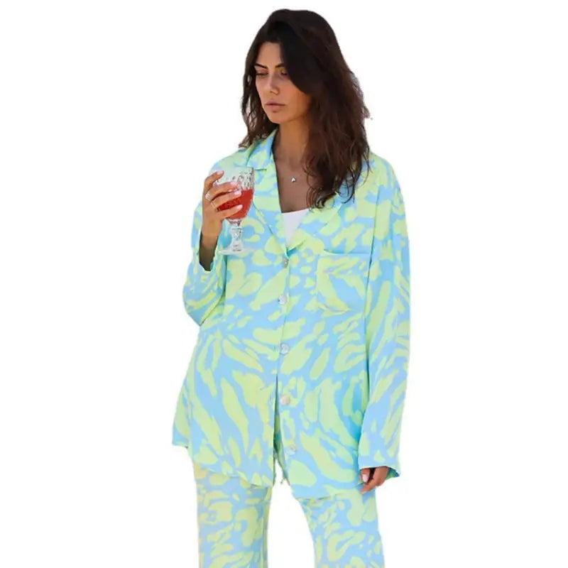 Woman in patterned elegance silk pajamas holding a drink showcasing long sleeve silk pajamas