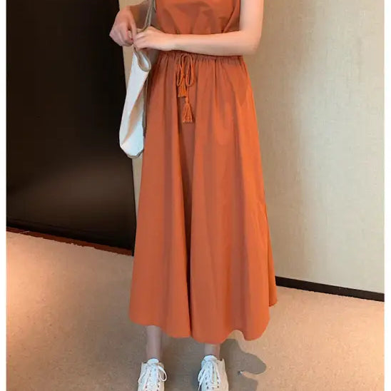 Orange maxi dress with cap sleeves and a drawstring waist, paired with white sneakers and a shoulder bag.