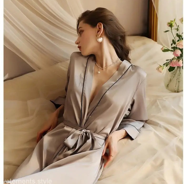 Elegant woman in tied waist midi silk pajamas sitting on bed, perfect for spring fall