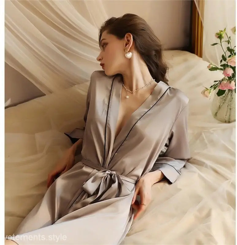 Elegant woman in tied waist midi silk pajamas sitting on bed, perfect for spring fall