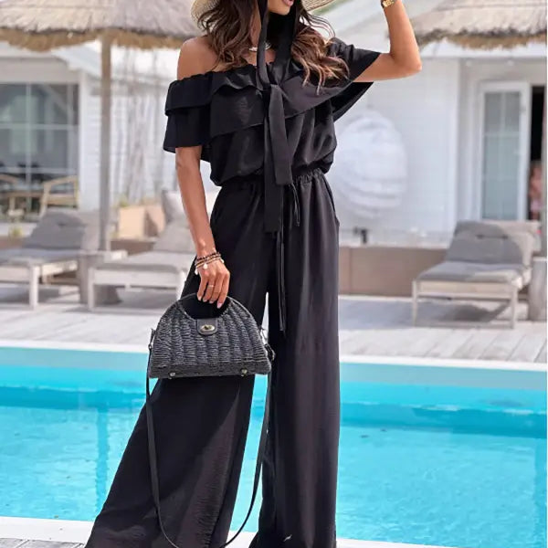 Woman in black off shoulder jumpsuit and straw hat, featuring elegant ruffle design