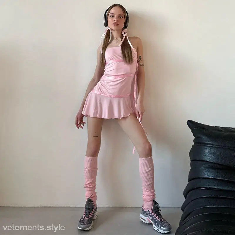 Young woman in pink showcasing a ribbon ruffled dress with leg warmers and headphones