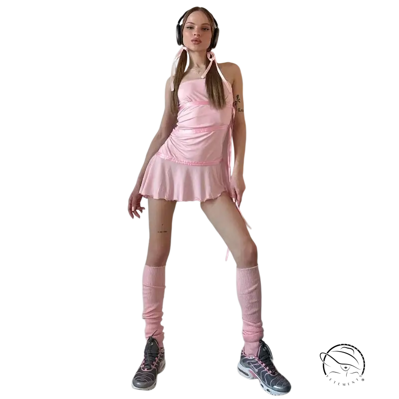 Young woman in ruffled sexy strapless dress, pink outfit with leg warmers and headphones against wall