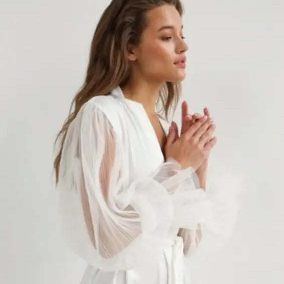 Woman with long brown hair wearing an elegant silk loose nightgown with sheer sleeves