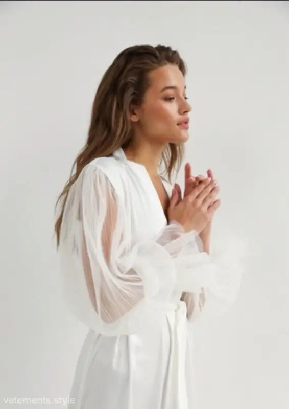 Woman with long brown hair wearing an elegant silk loose nightgown with sheer sleeves