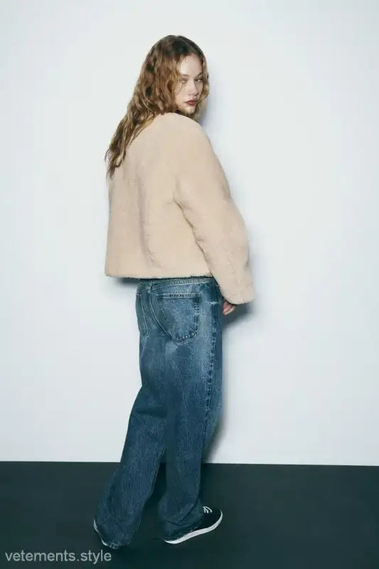 Woman in beige ornament fleece jacket, blue jeans, looking over her shoulder