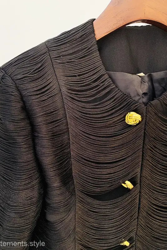 Textured black jacket with yellow rose-shaped buttons hanging on a wooden hanger, stylish tassel short jacket