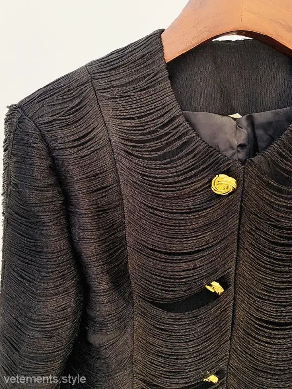 Textured black jacket with yellow rose-shaped buttons hanging on a wooden hanger, stylish tassel short jacket
