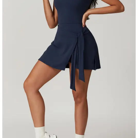 Navy blue sleeveless mini dress with a pleated skirt detail worn with white socks and chunky sneakers.