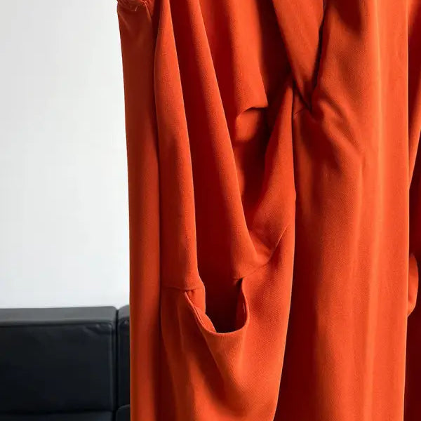 Bright orange flowing fabric garment with draped folds and a pocket.