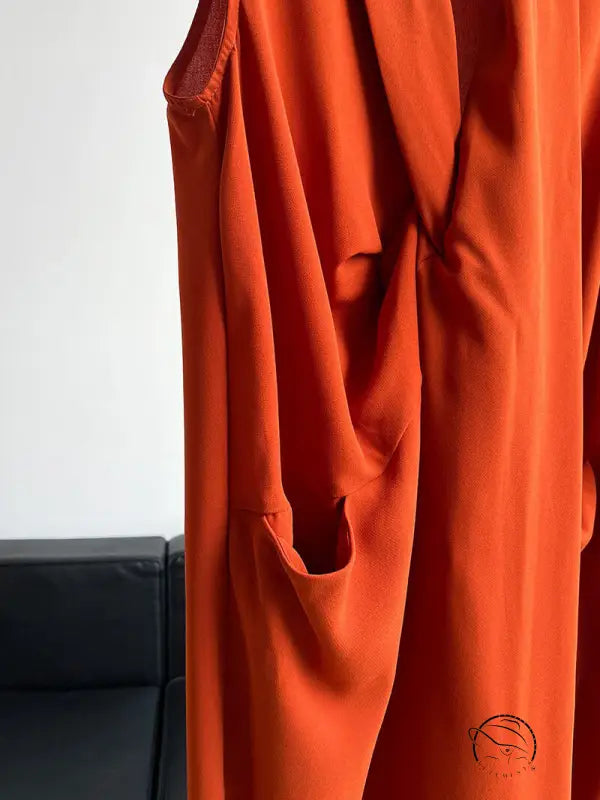 Elegant V-neck long dress in bright orange flowing fabric with draped folds and pockets