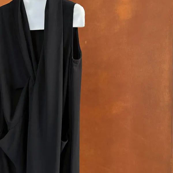 Black sleeveless wrap dress or top hanging on a white hanger.